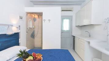 Habitación de hotel con cama, bandeja de desayuno con frutas, ducha, lavamanos y ventana.