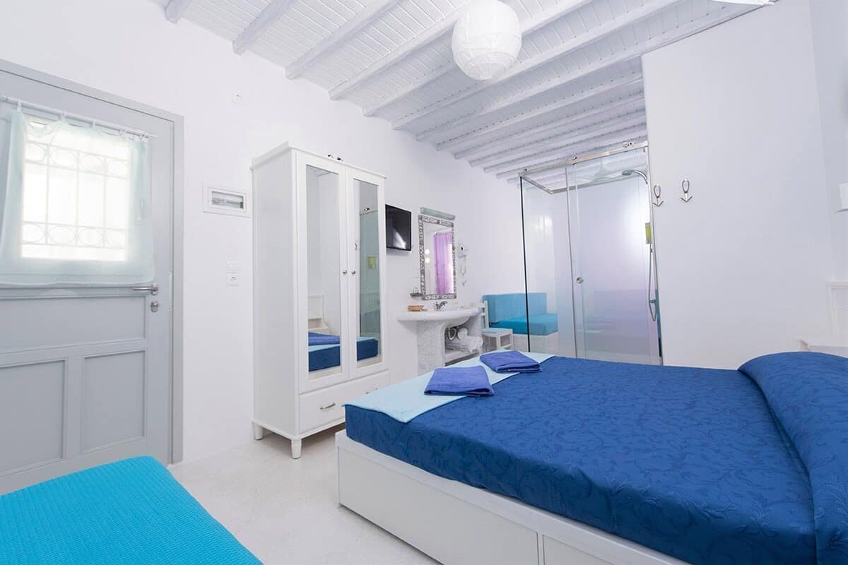 A bedroom with a bed, a wardrobe, a vanity, and a shower.