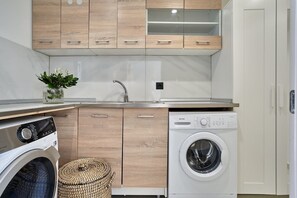 A compact kitchen with wooden cabinets, a built-in washing machine, and a sink. - Sia Mare Residence (Rhodes)