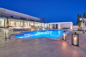 A swimming pool with a curved edge, surrounded by lounge chairs and a modern building with large windows. - Sia Mare Residence (Rhodes)