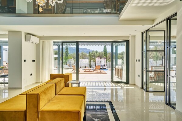 Un interior moderno con un sofá, una puerta de cristal que da a un área exterior con piscina y mobiliario.
