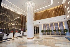 Eine moderne Hotelhalle mit einer Rezeption, einer großen Zierensäule und einer Wand mit Muster.