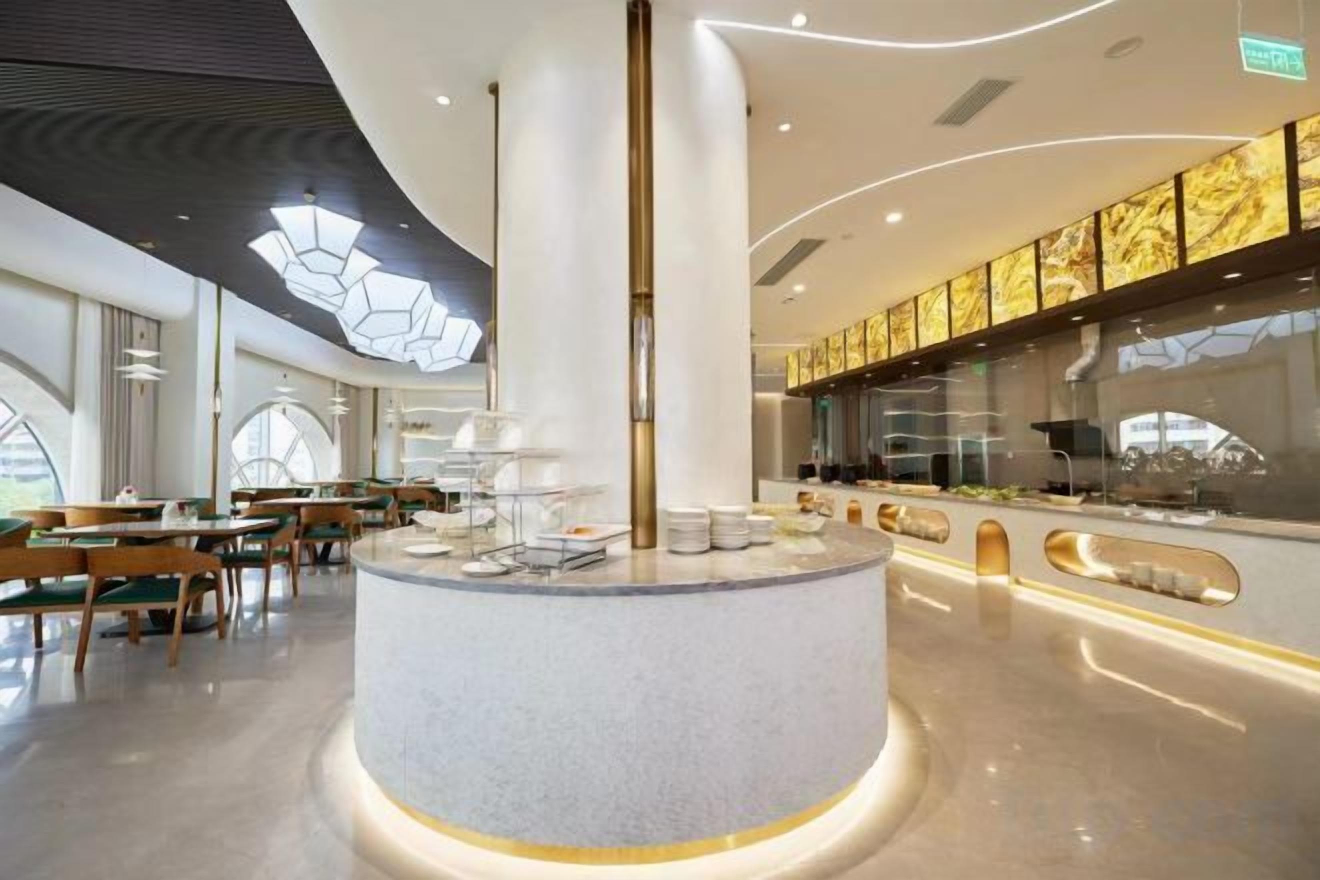 A modern hotel lobby with a central round bar, seating areas, and a large window providing natural light.