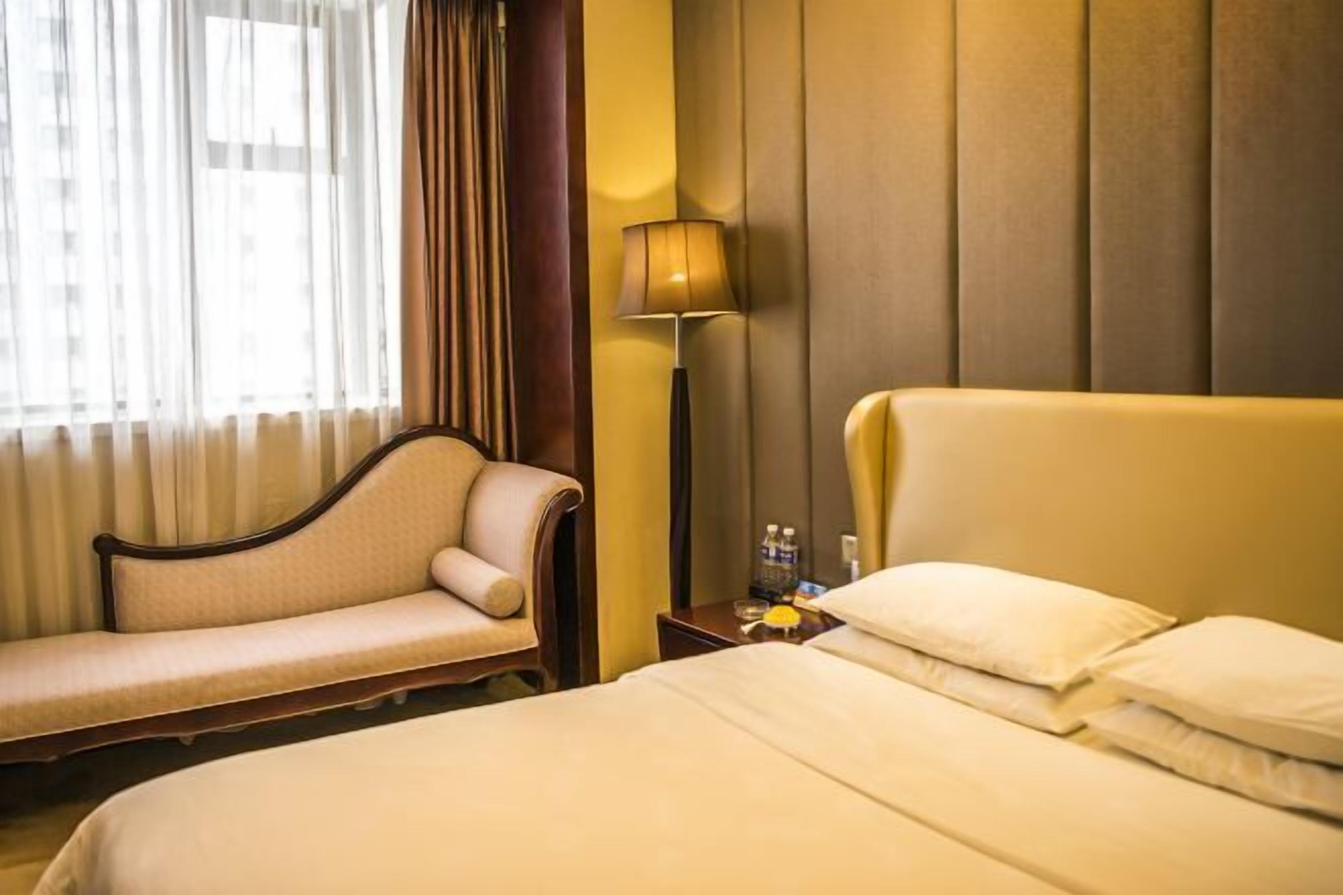 A hotel room with a bed, a sofa, a lamp, and a window with curtains.