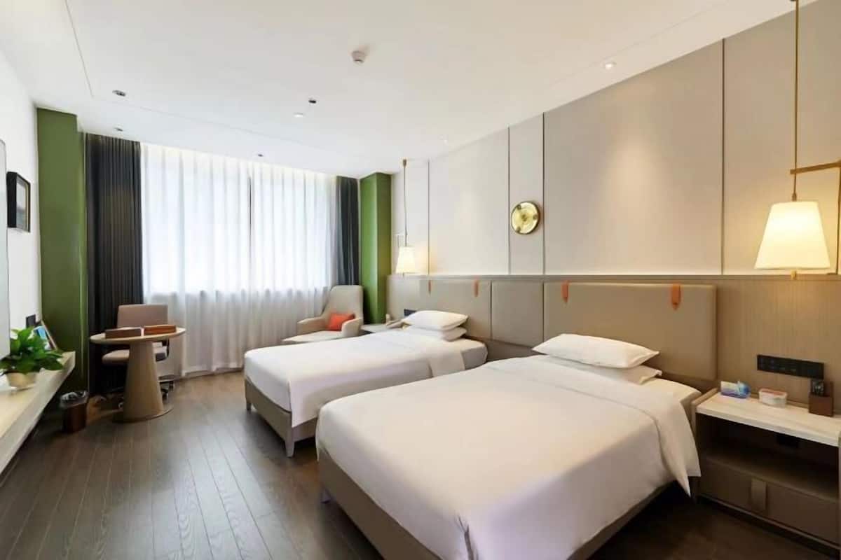 Hotellihuone, jossa on kaksi sänkyä, työpöytä, tuoli, lamppu ja seinäkello.