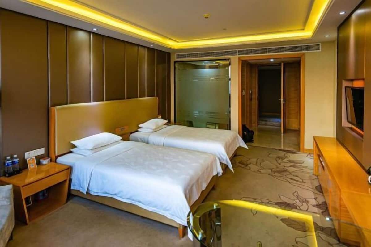 Hotellihuone, jossa on kaksi sänkyä, puinen työpöytä, televisio ja kylpyhuone, jossa on lasiovi.