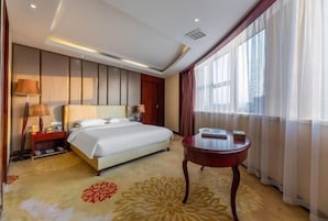 Habitación de hotel con cama, mesitas de noche, lámpara, una pequeña mesa y ventana con cortinas.