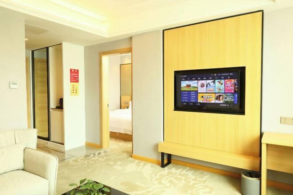 Une chambre d’hôtel équipée d’un téléviseur à écran plat fixé au mur, d’un canapé, d’un lit et d’une petite poubelle.