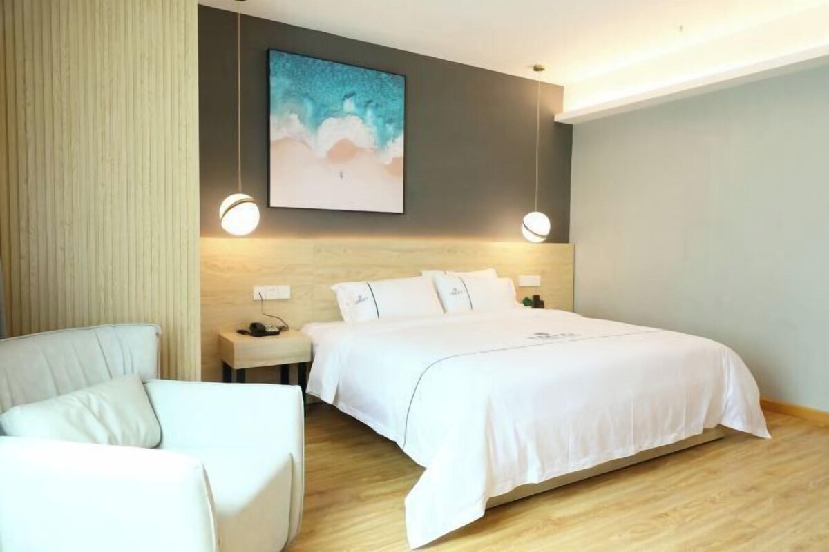 A modern hotel room with a large bed, a bedside table, a chair, and a painting on the wall.