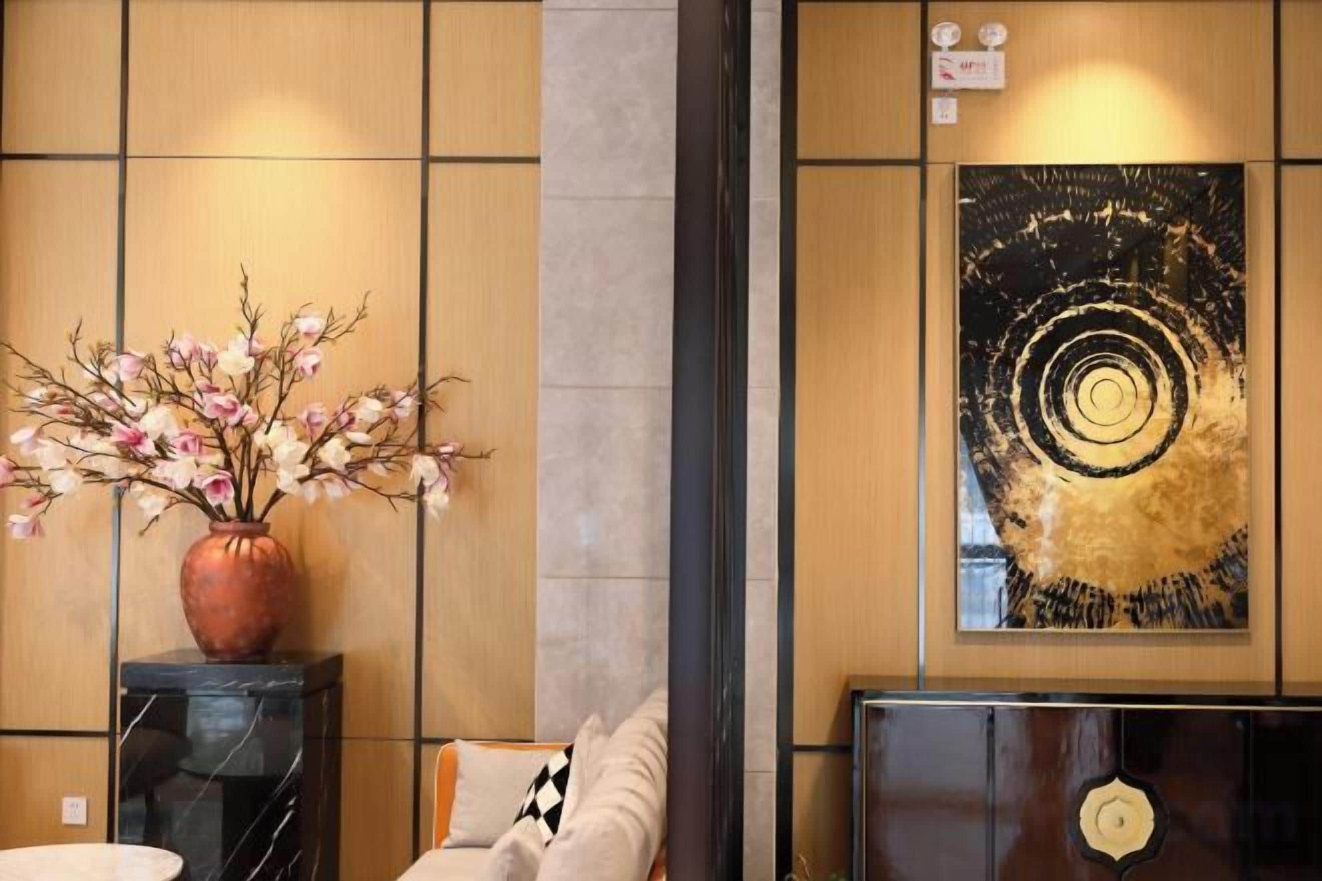 A reception area with a vase of flowers, a black console table, a sofa, and a large abstract painting on the wall.