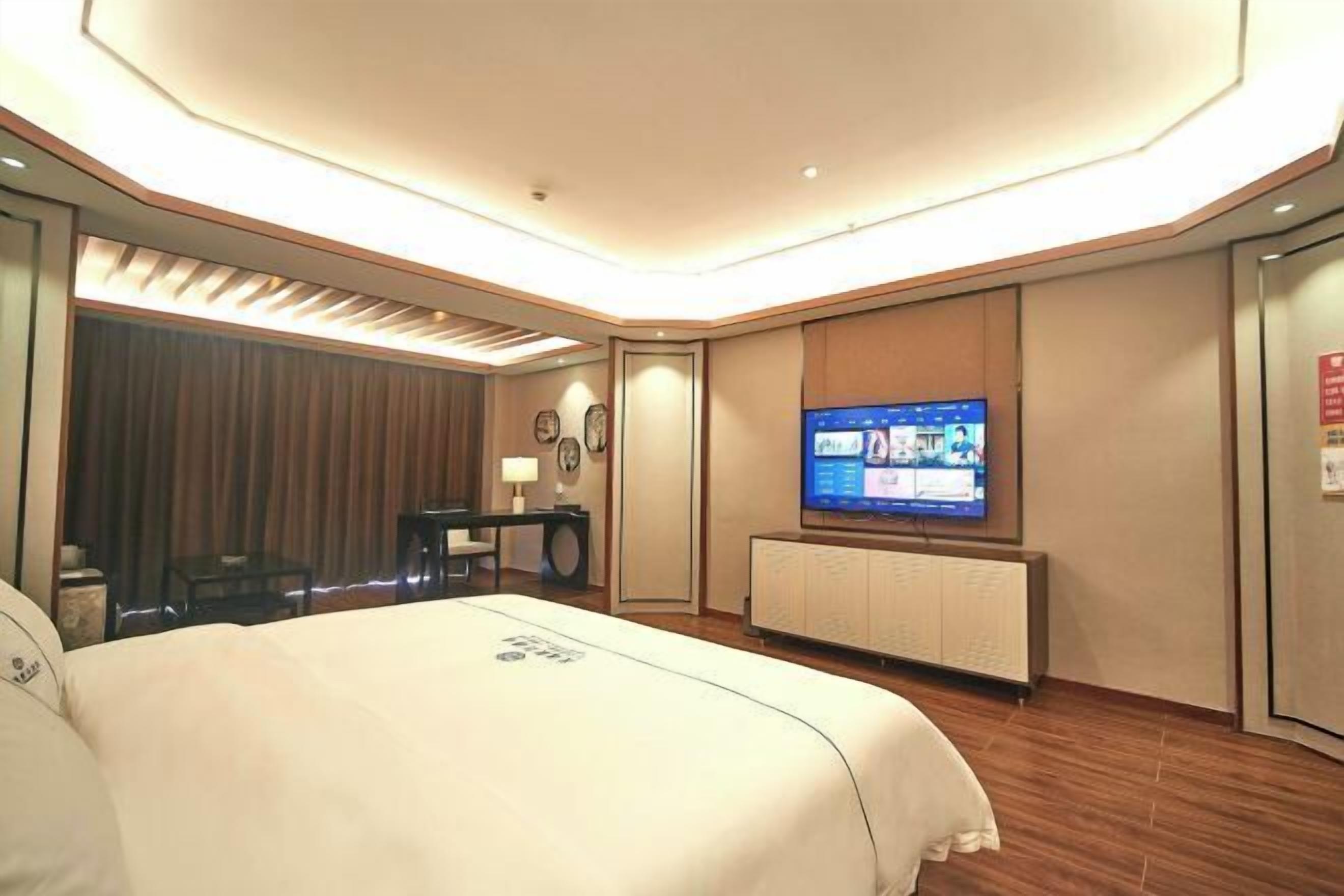 A hotel room with a large bed, a desk, a television, and a wall-mounted cabinet.