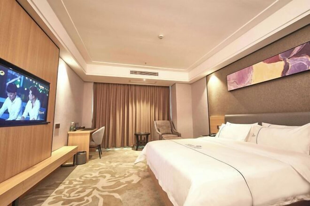 A hotel room with a large bed, a desk, a chair, a TV, and a painting on the wall.