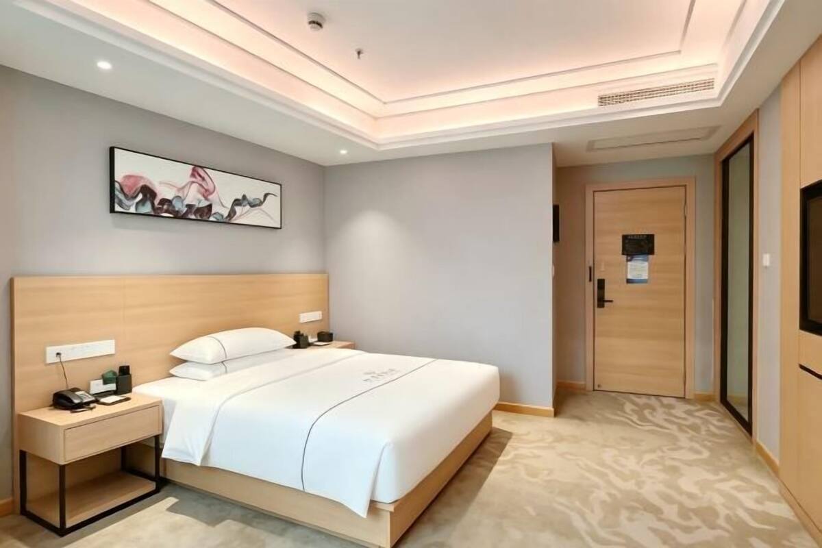Une chambre d’hôtel comprenant un lit, des tables de chevet, une commode, une œuvre d’art accrochée au mur, une porte et un téléviseur.