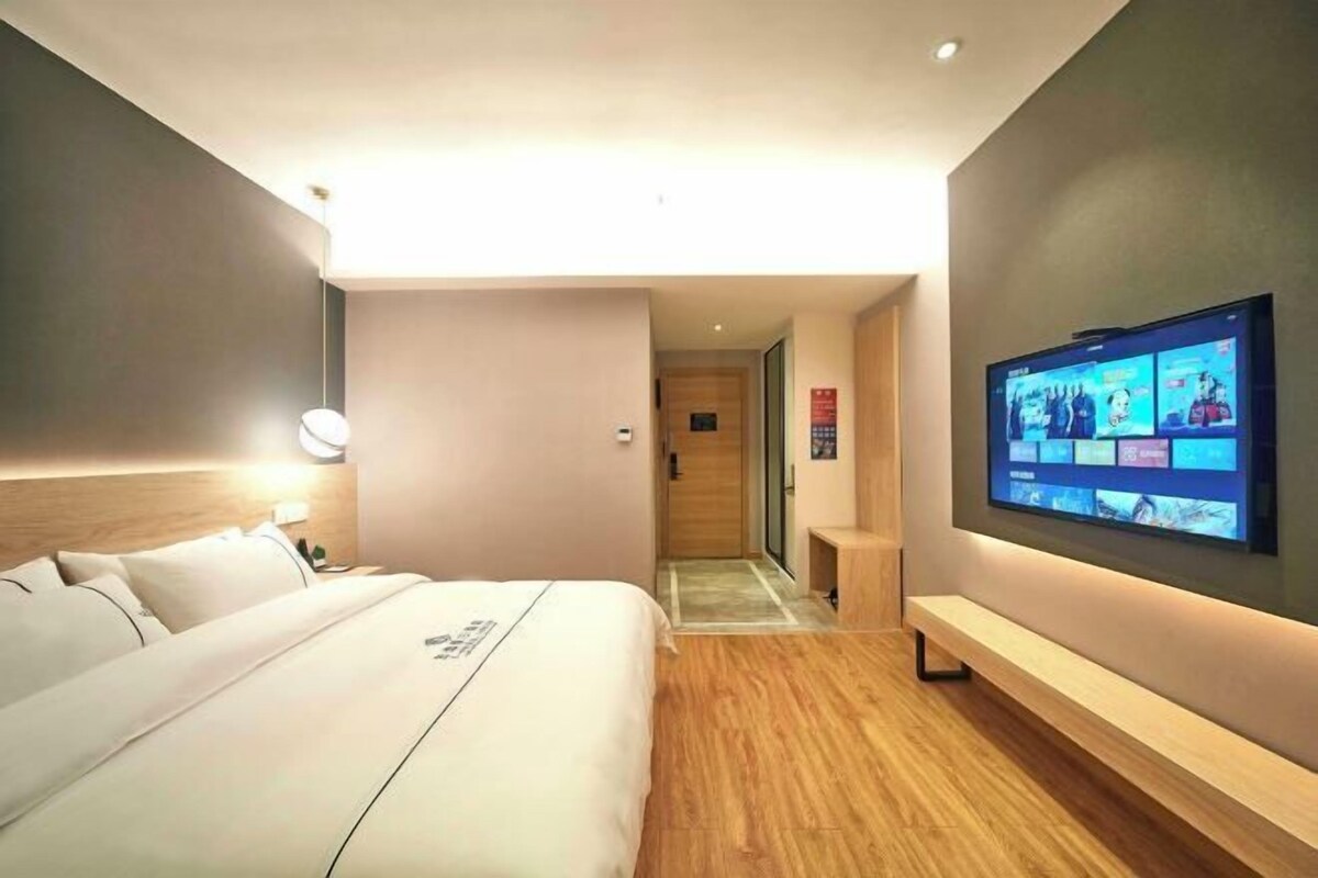 A modern hotel room with a large bed, a TV mounted on the wall, and a wooden floor.