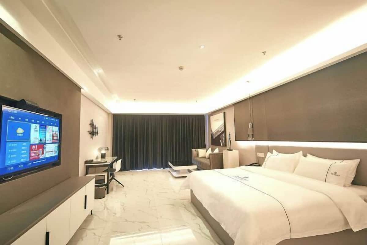 A modern hotel room with a large bed, a desk with a computer, a flat-screen TV, and a large window with curtains.