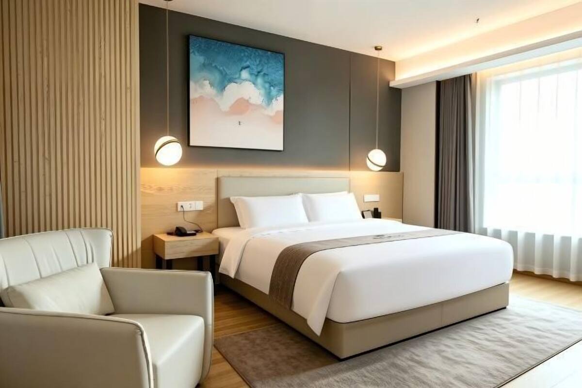 Une chambre d’hôtel moderne avec un grand lit, une table de chevet, une chaise et un tableau au mur.