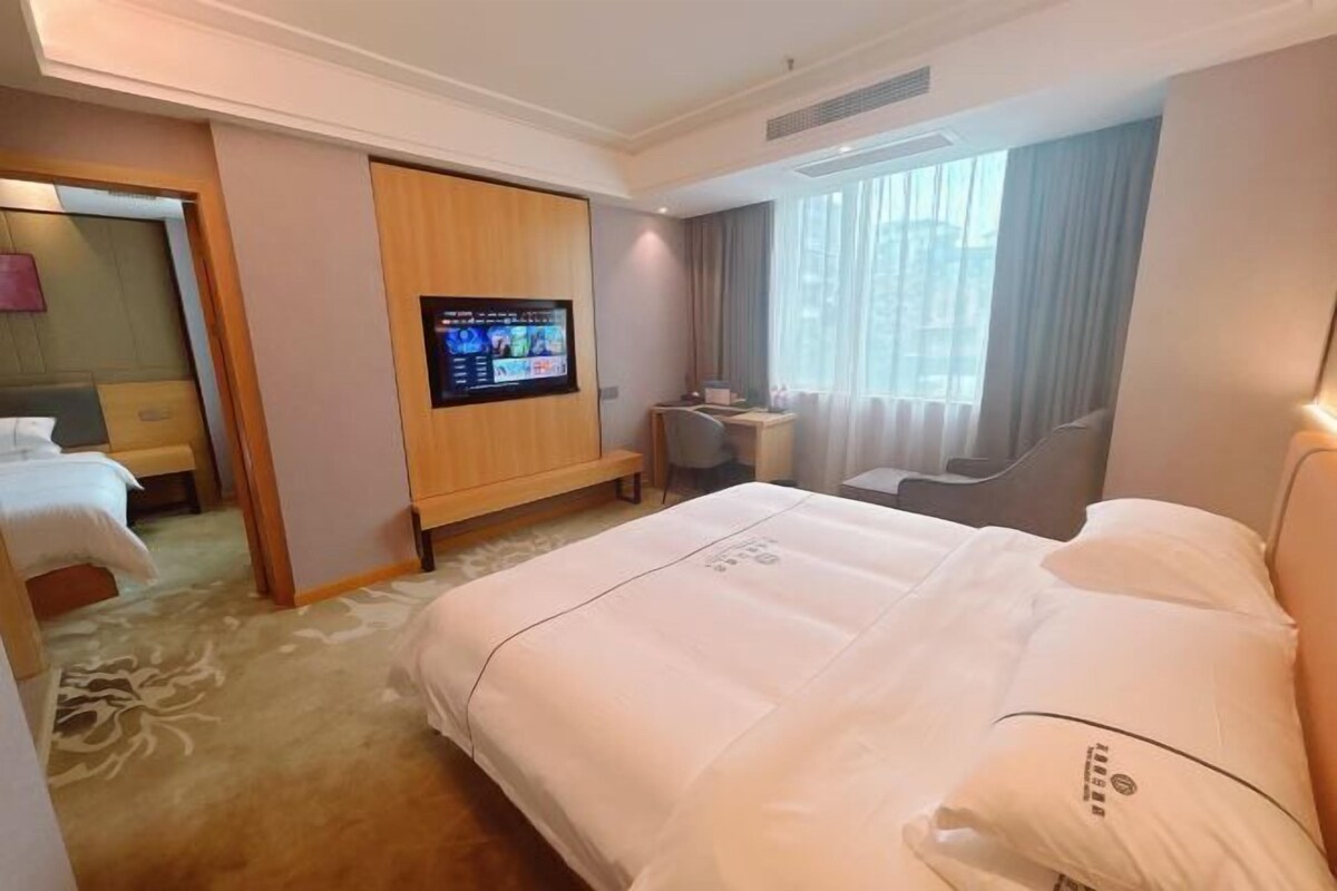 A hotel room with a large bed, a desk, a television, and a view of the city through the window.