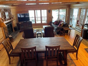 Een gezellig interieur van een chalet met een houten eettafel, stoelen, een bank en een televisie.