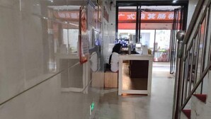 Zona de recepción con mostrador, escalera y puerta de vidrio que da a otra habitación.