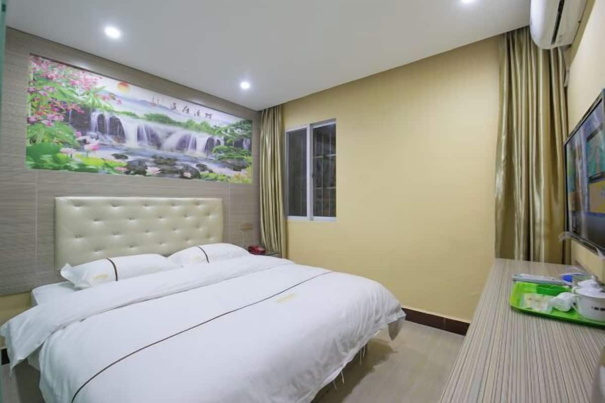 A hotel room with a large bed, a mural of a waterfall, a window, and a TV on a desk.