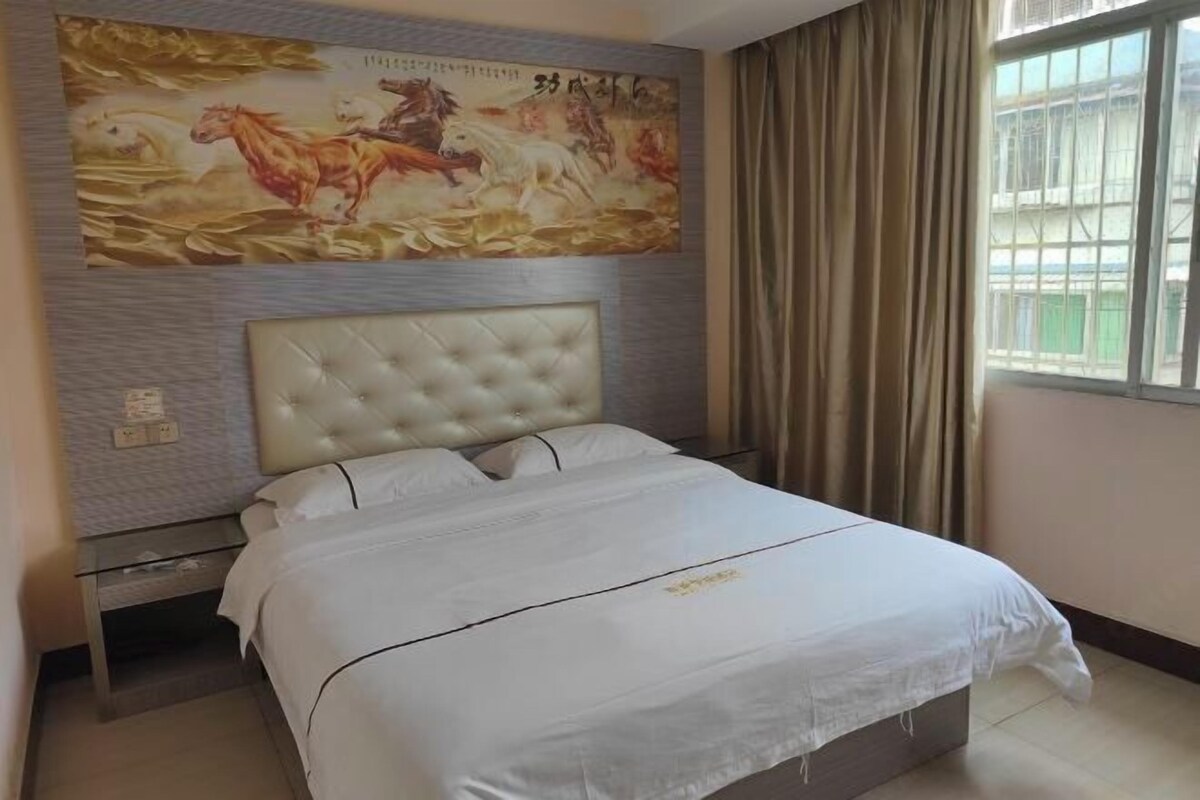 A hotel room with a large bed, a headboard, a wall with a mural, a window with curtains, and a nightstand.