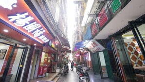 Una calle estrecha con comercios a ambos lados, una acera para peatones y scooters estacionados.