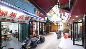 Vista de la calle con un restaurante llamado 'Xiazhou Wind Flavor' y una farmacia. Hay scooters estacionados afuera y una bicicleta a la izquierda.