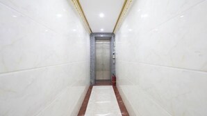 Un estrecho pasillo con paredes de mármol blanco y suelo de mármol rojo que conduce a un ascensor.