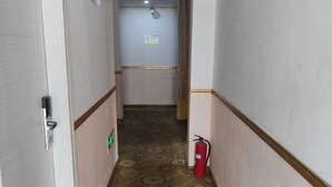 Un pasillo estrecho con alfombra estampada, un extintor y una puerta a la izquierda.