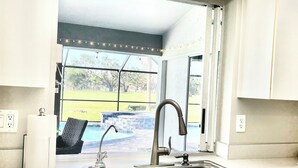 A kitchen with a double sink, a dish rack, a paper towel holder, and a view of a backyard with a hot tub. - Stunning Sunsets-Heated Pool and Spa-Golf Course Views (Cape Coral)