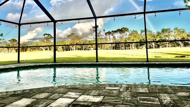 A pool area with a view of a golf course through a large window structure. - Stunning Sunsets-Heated Pool and Spa-Golf Course Views (Cape Coral)