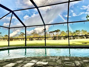 Zona de piscina con vista a un campo de golf a través de una estructura de grandes ventanales.