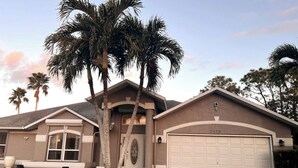 A single-story house with a garage, palm trees, and a clear sky. - Stunning Sunsets-Heated Pool and Spa-Golf Course Views (Cape Coral)