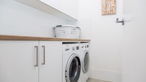 A modern laundry room with white cabinets, a wooden countertop, and two Bosch washing machines. - Salt and Light Mollymook (Mollymook Beach)