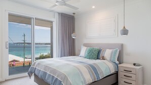A bedroom with a large sliding glass door leading to a balcony with a view of the sea. - Salt and Light Mollymook (Mollymook Beach)