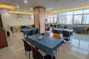 A dining area with tables and chairs, a pillar, and a window with a view. - Tomato Hotel (Dongguan)