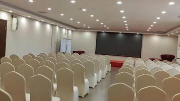 Un salón de conferencias con filas de sillas, una pantalla de proyector y una pizarra.