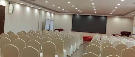 A conference room with rows of chairs, a projector screen, and a whiteboard.