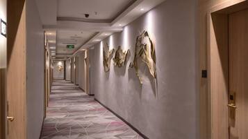 Ein Hotel-Flur mit einem geometrisch gemusterten Teppich, Wandbildern und Holztüren.