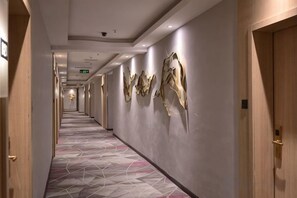 A hotel hallway with a geometric patterned carpet, wall-mounted artwork, and wooden doors. - Tomato Hotel (Dongguan)