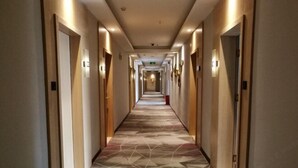 A long, narrow hotel corridor with a patterned floor, doors on both sides, and overhead lighting. - Tomato Hotel (Dongguan)