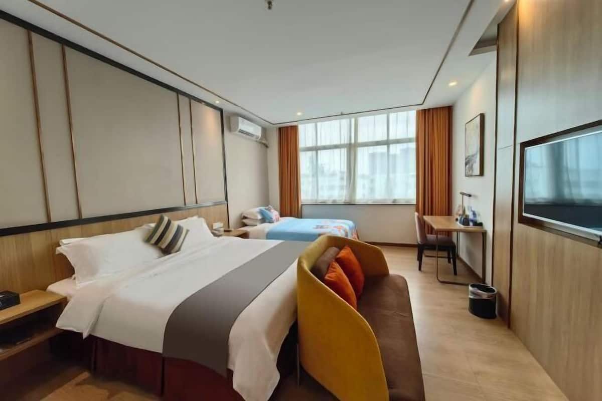 A hotel room with a bed, a sofa, a desk, a TV, and a window.