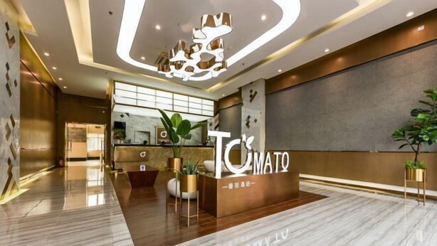 A modern hotel lobby with a reception desk, a large mirror, and a decorative ceiling light. - Tomato Hotel (Dongguan)