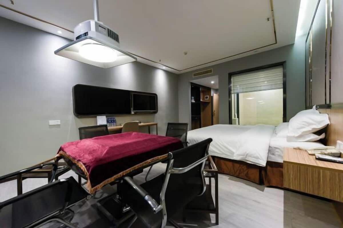 A hotel room with a bed, bedside table, chair, desk, flat-screen TV, and a ceiling-mounted light fixture.