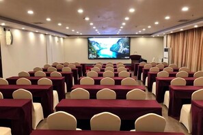 A conference room with rows of tables and chairs, a screen, and a podium. - Tomato Hotel (Dongguan)