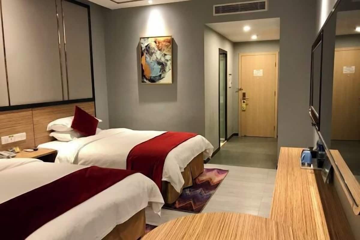 A hotel room with two beds, a wooden desk, a mirror, and a painting on the wall.