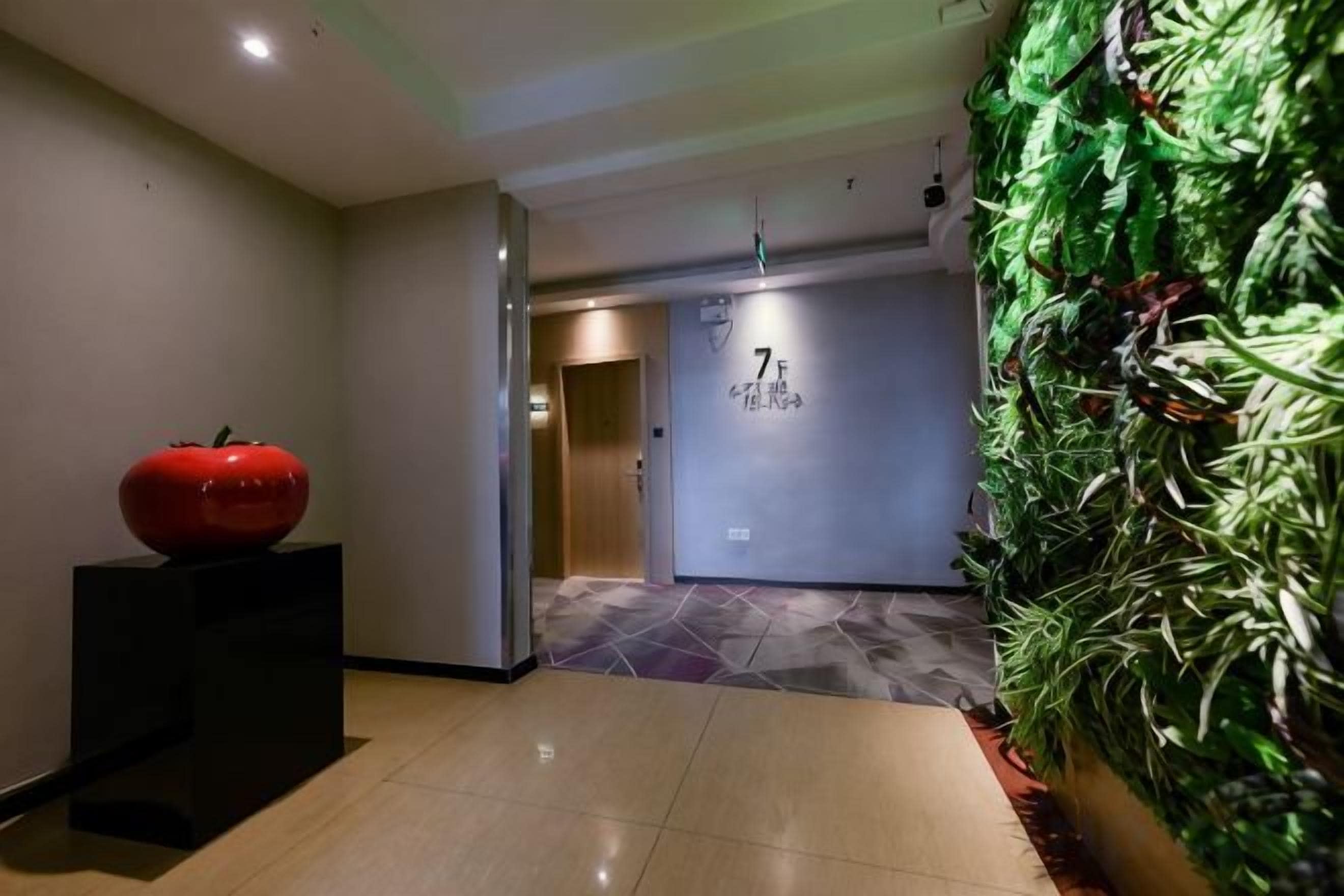 A hallway with a red apple sculpture, a wall with a number sign, and a vertical garden.
