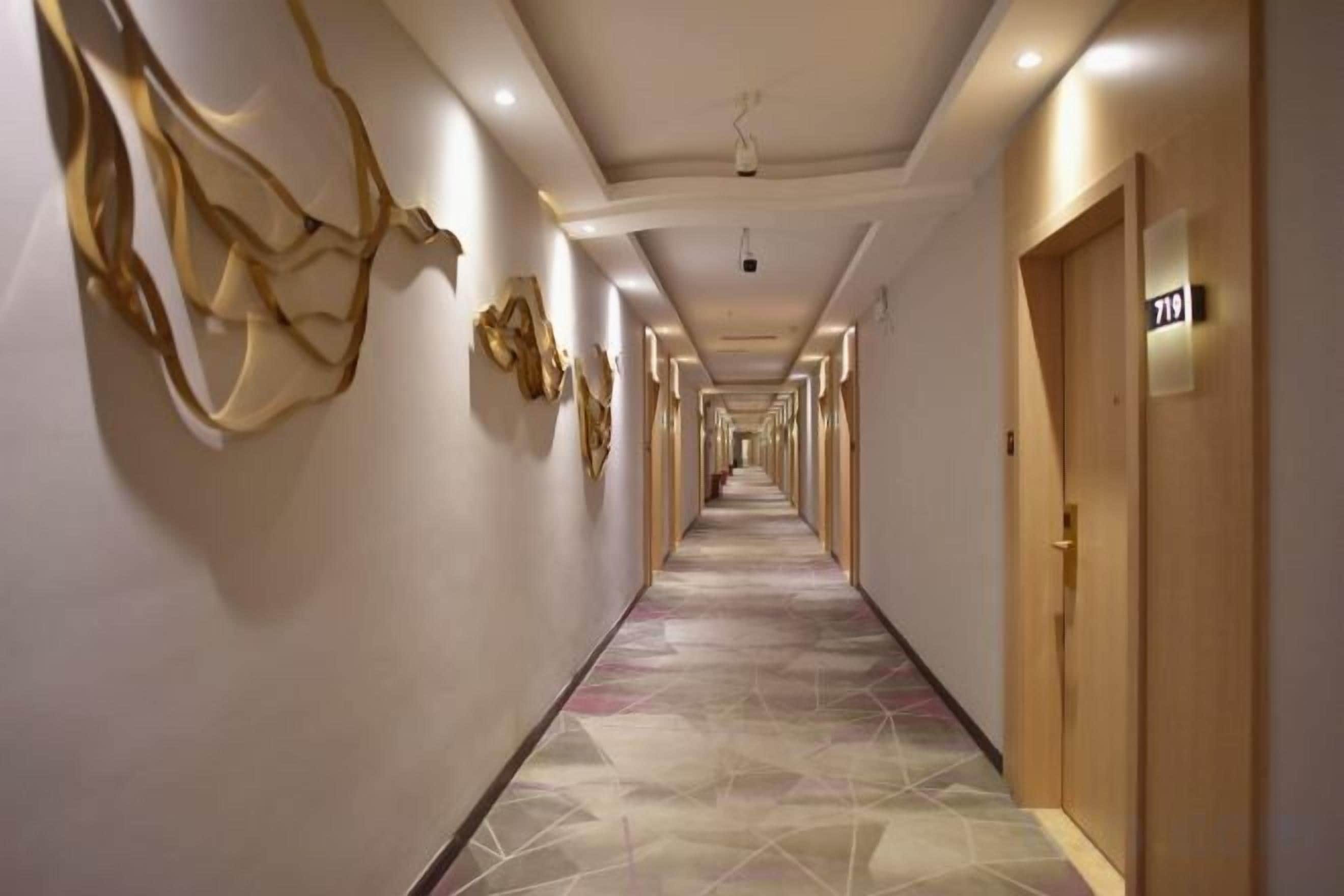 A hotel corridor with doors, a patterned floor, and wall art.