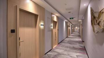 Corredor de hotel com portas de madeira, carpete estampado e luminárias fixadas na parede.