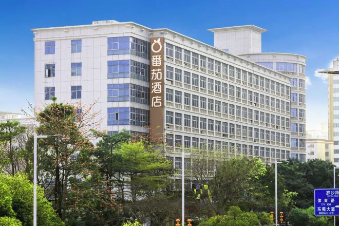 A multi-story hotel with a prominent vertical sign, surrounded by greenery and other buildings.